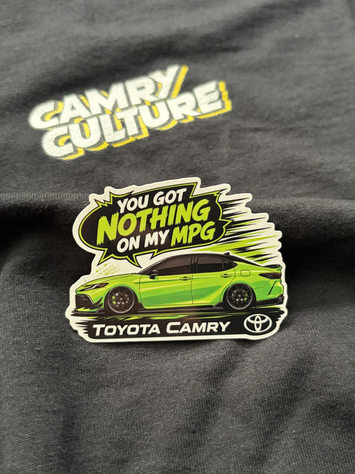 A die-cut sticker featuring a bright green Toyota Camry car and the text 'YOU GOT NOTHING ON MY MPG' with 'TOYOTA CAMRY' and the Toyota logo, displayed on a black t-shirt with a 'Camry Culture' graphic.
