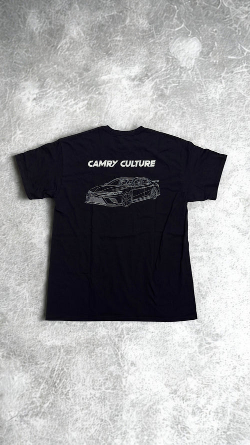 A black short-sleeve t-shirt laid flat on a textured gray concrete background. The back of the shirt features a white graphic print of a sports car and the text 'CAMRY CULTURE'.