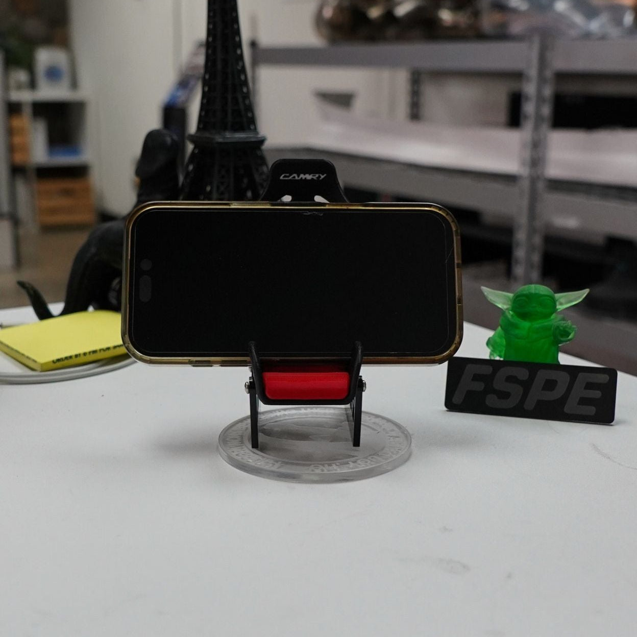 Phone holder holding phone on a white desk surrounding by other items on the desk