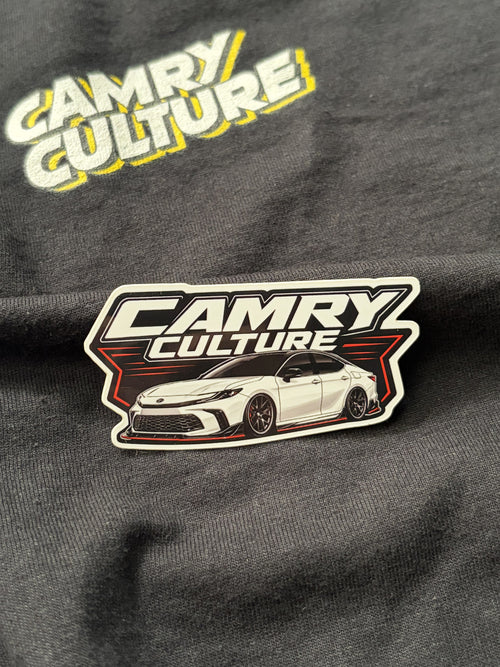 Close up of a "Camry Culture" white retro sticker sitting on top of a black shirt that has the Camry Culture logo. The camry is a XV80 lowered. 